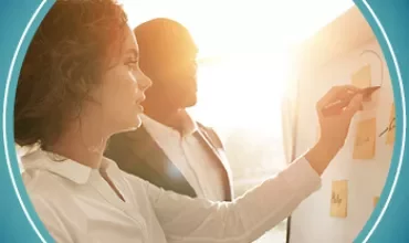 Two people collaborating at a board with sticky notes in sunlight.